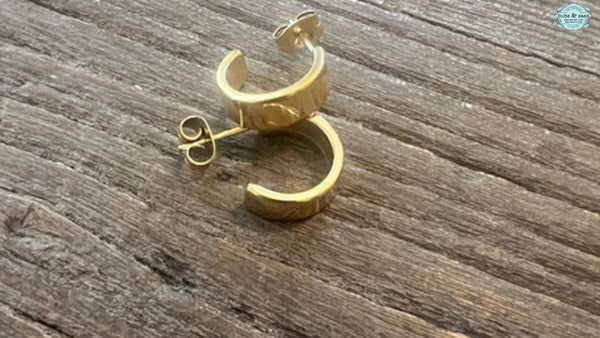 A pair of elegant gold earrings displayed on a rustic wooden table.